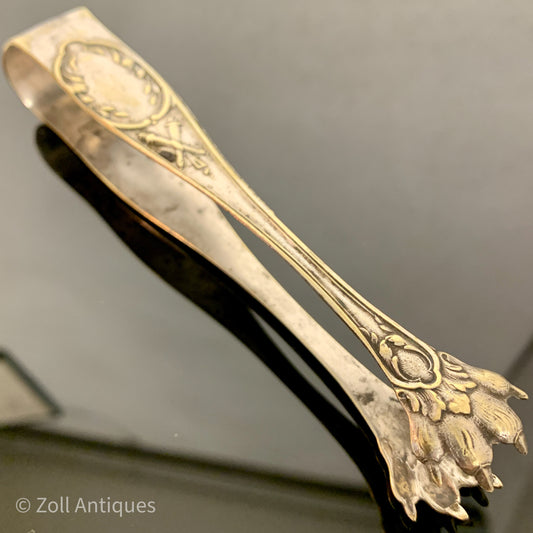 Et antik sølvbelagt sukker tang, der er lavet af metal og har en ornamenteret design. Det er et vintage genstand, der er blevet br