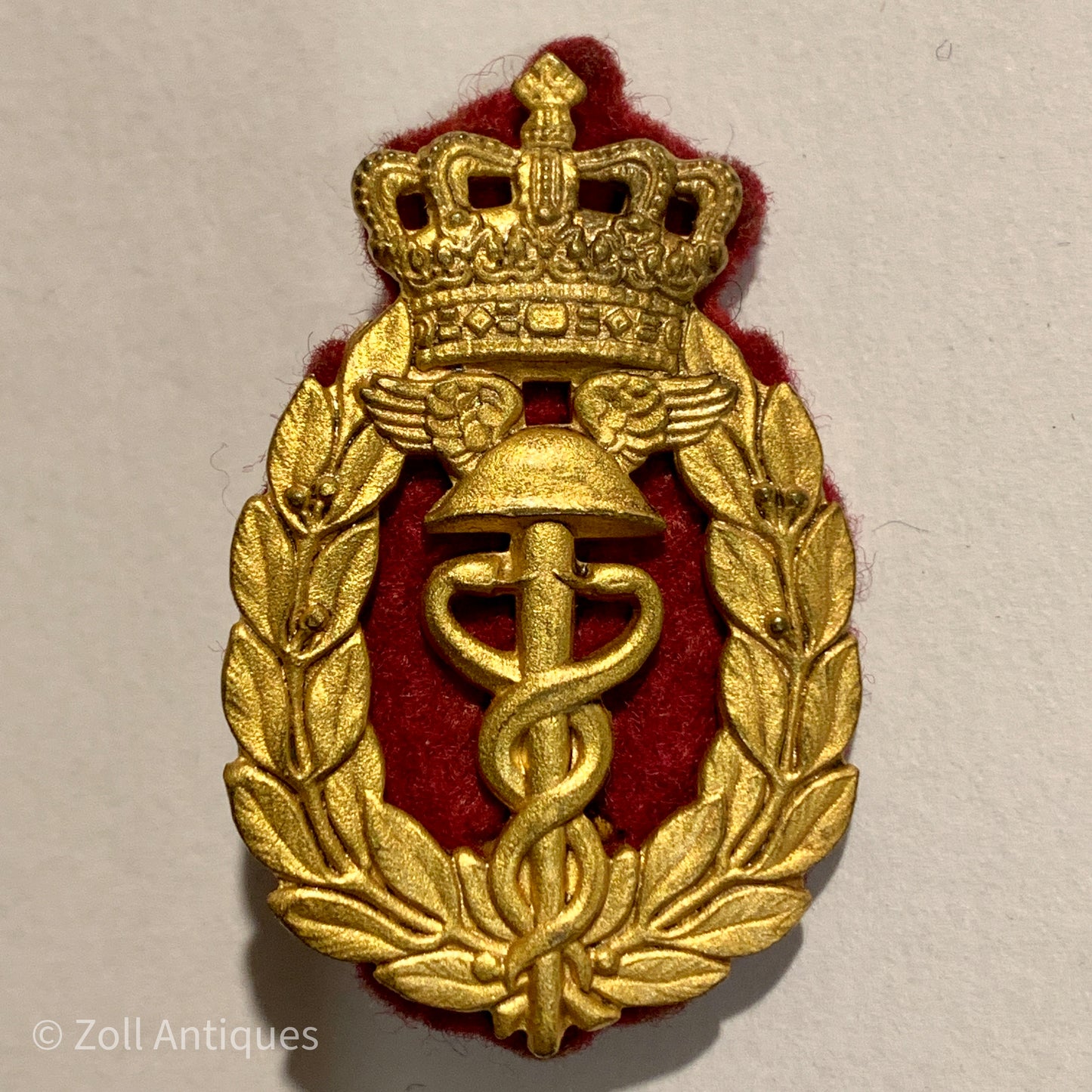 "Forsvarets intendanturkorps mærke" er et vintage emblem, der viser en kronet krone og et kors. Emblemmet er lavet af guld og er u